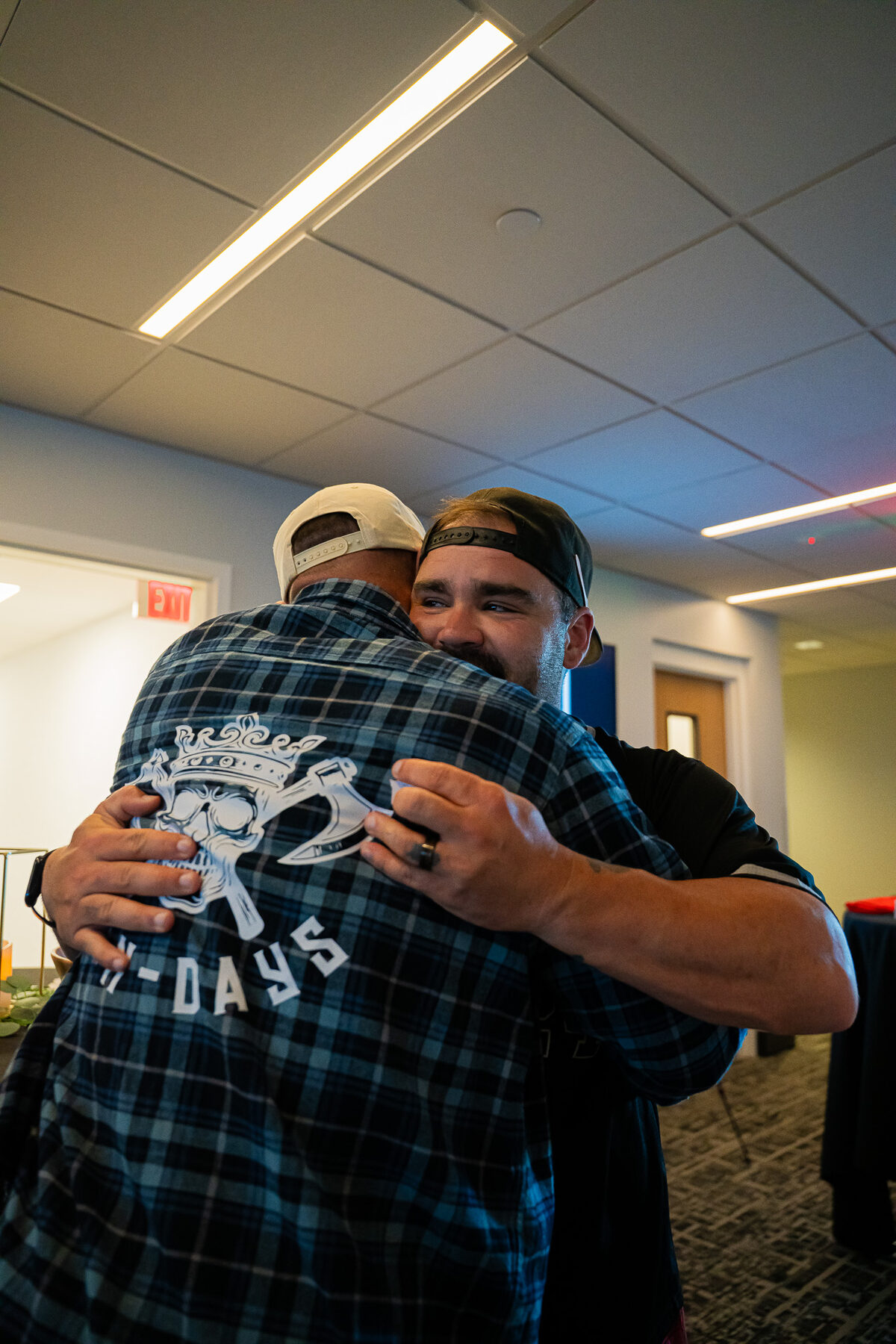 Two men sharing a strong embrace at a Man Days Project event, one wearing a Man Days shirt, in a moment of genuine brotherhood and support