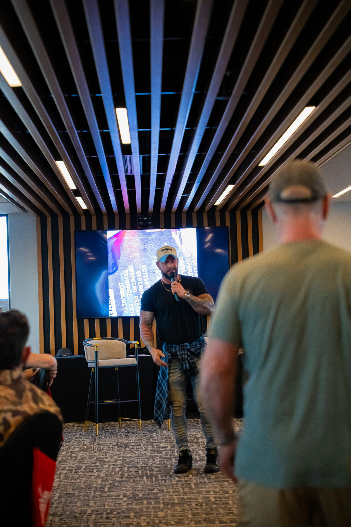 A Man Days Project leader speaking with a microphone to a room of men gathered at a community event